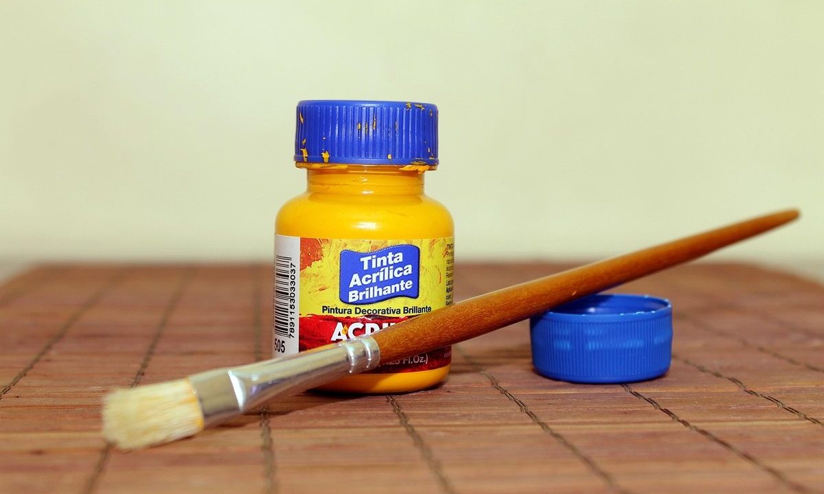 Une bouteille d'acrylique jaune, un pinceau et son cap sur une table en bois