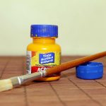 Une bouteille d'acrylique jaune, un pinceau et son cap sur une table en bois