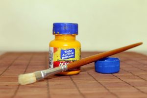 Une bouteille d'acrylique jaune, un pinceau et son cap sur une table en bois