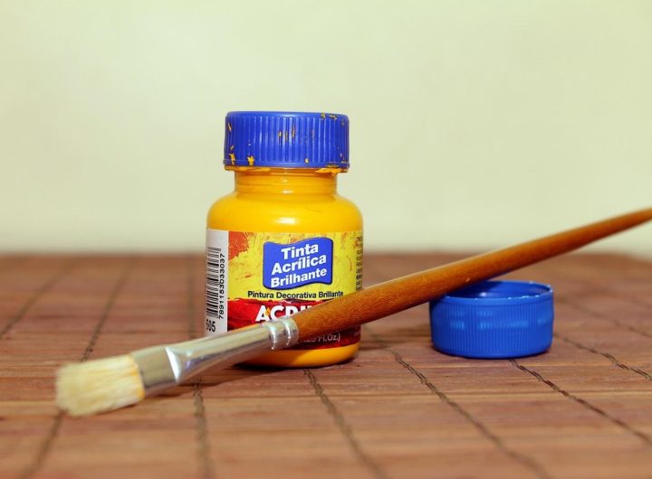 Une bouteille d'acrylique jaune, un pinceau et son cap sur une table en bois