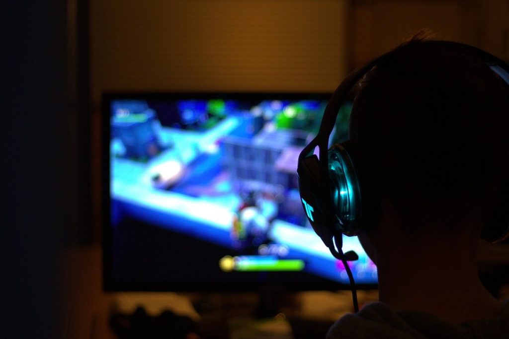 Une personne en silhouette porte un casque et regarde un écran de jeu vidéo
