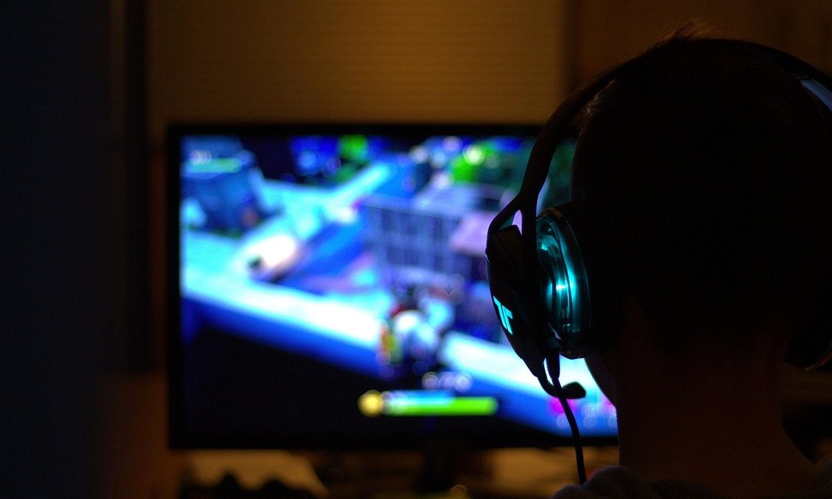 Une personne en silhouette porte un casque et regarde un écran de jeu vidéo
