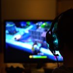 Une personne en silhouette porte un casque et regarde un écran de jeu vidéo