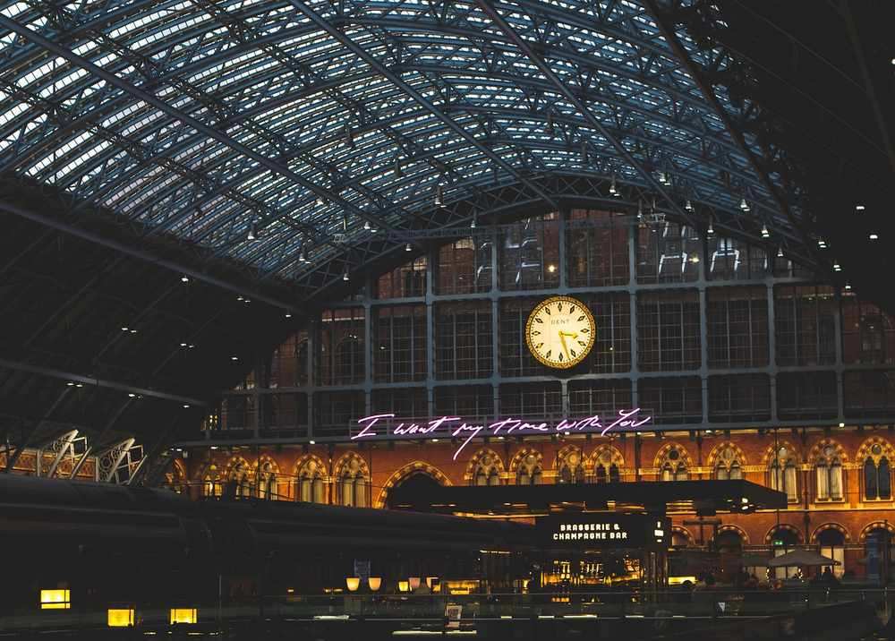 Intérieur d'une gare avec un toit en verre, une horloge, des lumières et des inscriptions Intérieur d'une gare avec un toit en verre, une horloge, des lumières et des inscriptions