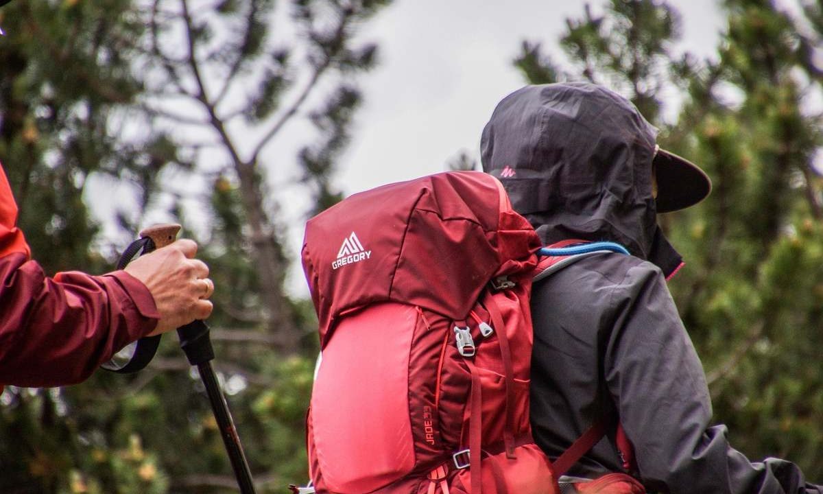Deux randonneurs avec des sacs à dos et des bâtons de marche en forêt sous un ciel nuageux