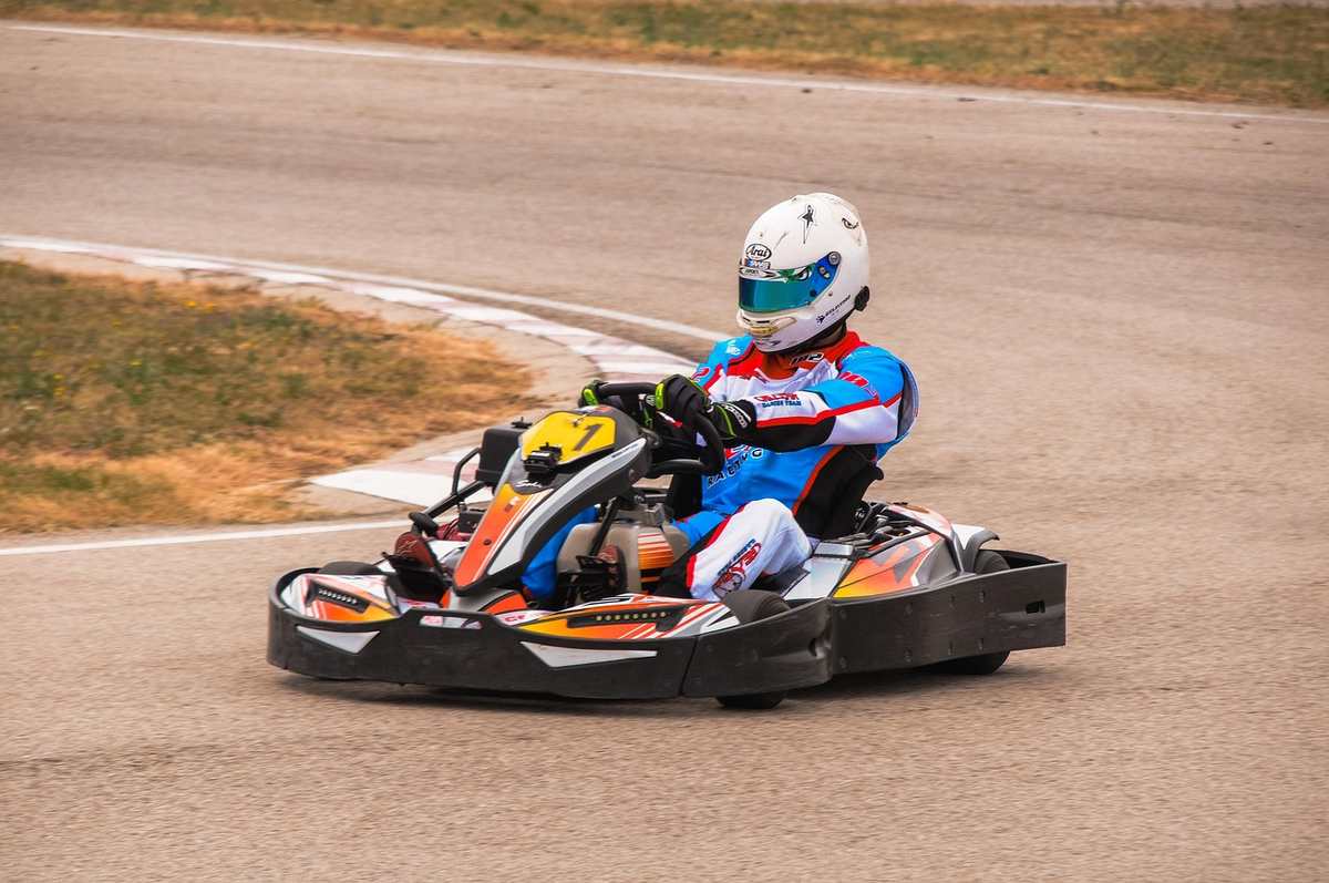 Un pilote en karting porte un casque blanc et conduit sur piste