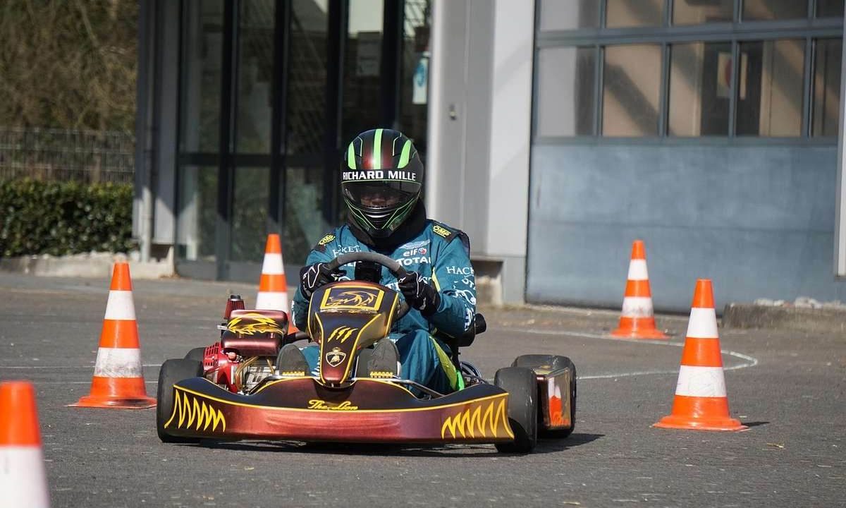 Pilote équipé d'un casque et de combinaison conduit un karting rouge et noir sur une piste délimitée par des cônes de signalisation