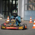 Pilote équipé d'un casque et de combinaison conduit un karting rouge et noir sur une piste délimitée par des cônes de signalisation