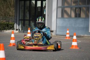 Pilote équipé d'un casque et de combinaison conduit un karting rouge et noir sur une piste délimitée par des cônes de signalisation