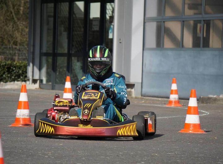 Pilote équipé d'un casque et de combinaison conduit un karting rouge et noir sur une piste délimitée par des cônes de signalisation