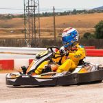 Pilote vêtu d'une combinaison jaune conduisant un kart sur une piste avec barrières rouges et blanches