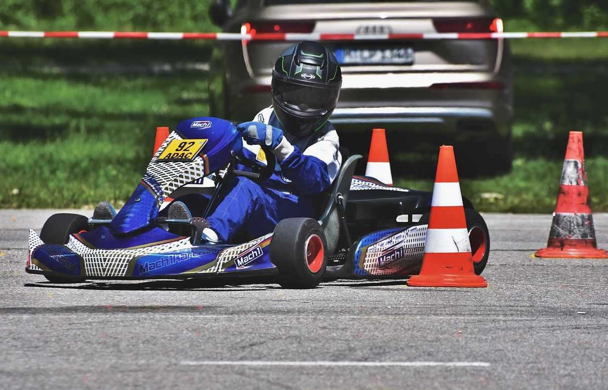 Un pilote en combinaison bleue conduit un kart de course entre cônes orange Un pilote en combinaison bleue conduit un kart de course entre cônes orange