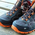 Paire de chaussures de randonnée avec lacets orange posée sur une surface en bois
