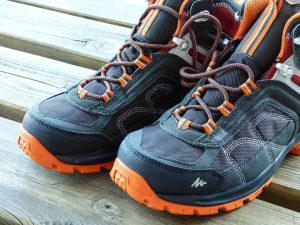 Paire de chaussures de randonnée avec lacets orange posée sur une surface en bois