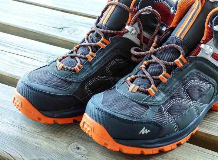 Paire de chaussures de randonnée avec lacets orange posée sur une surface en bois