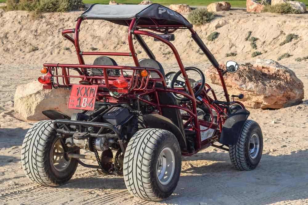 Un quadricycle rouge à quatre roues sur sable près d'un rocher Un quadricycle rouge à quatre roues sur sable près d'un rocher