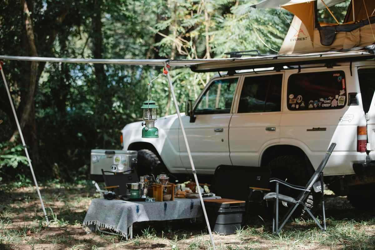 Camper blanc avec tente et matériel de camping dans une forêt Camper blanc avec tente et matériel de camping dans une forêt
