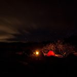 Campement de nuit en montagne avec tente rouge éclairée sous les étoiles