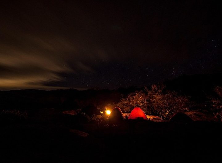 Campement de nuit en montagne avec tente rouge éclairée sous les étoiles