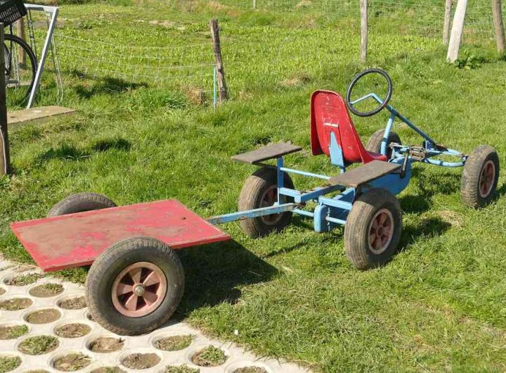Un kart bleu avec siège rouge tire une remorque sur gazon