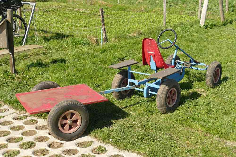 Un kart bleu avec siège rouge tire une remorque sur gazon